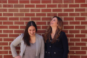 Two woman smiling in front of a brick wall